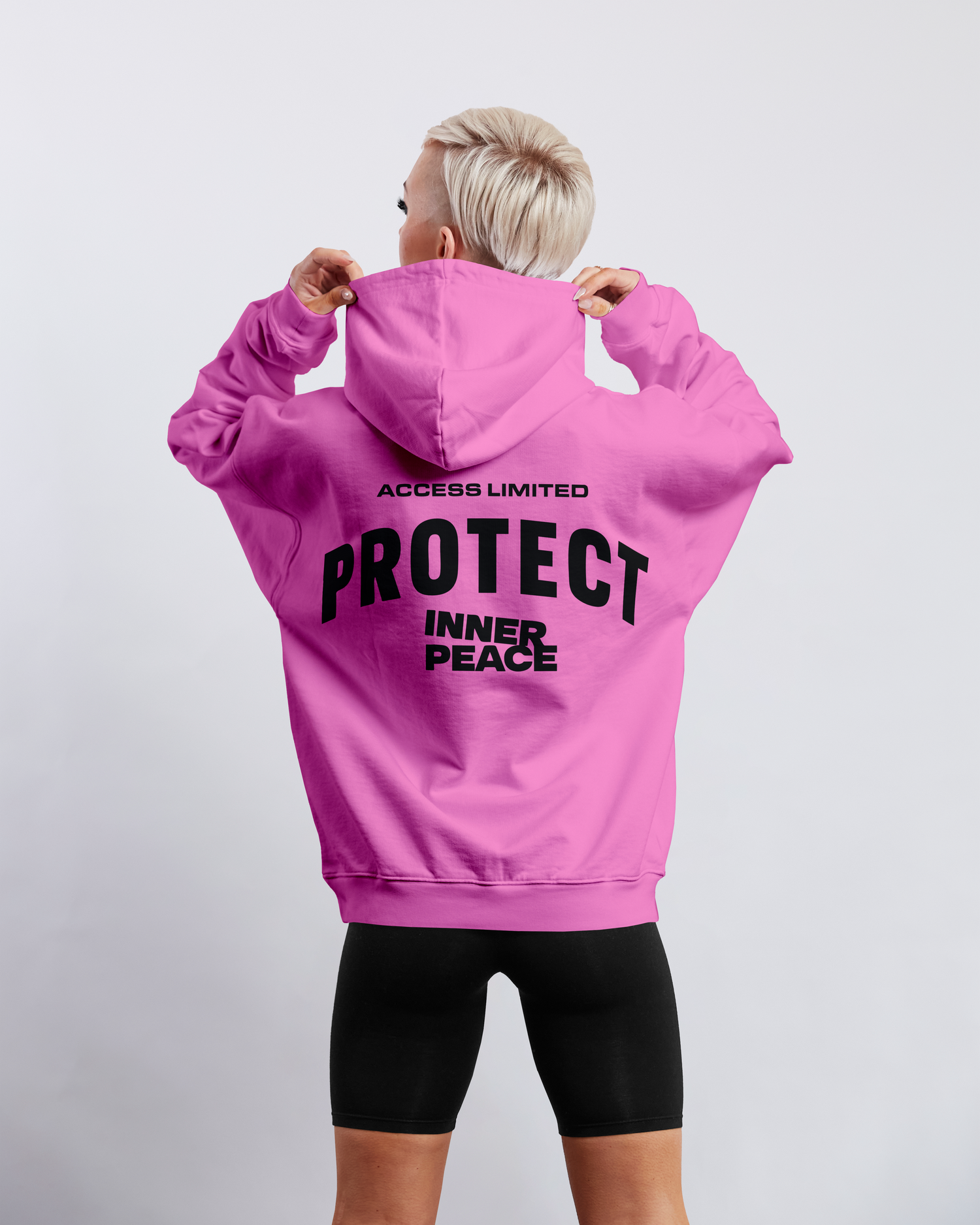 Model wearing a pink hoodie with 'Protect Inner Peace' print, showcasing women's fashion style.